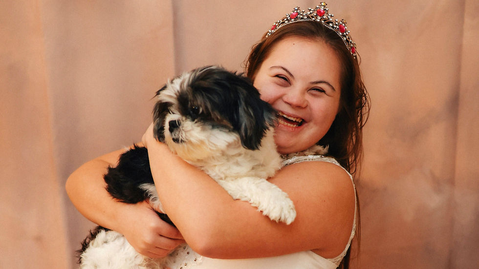 Smiling girl with Down syndrome in a jeweled tiara hugs a black-and-white fluffy dog